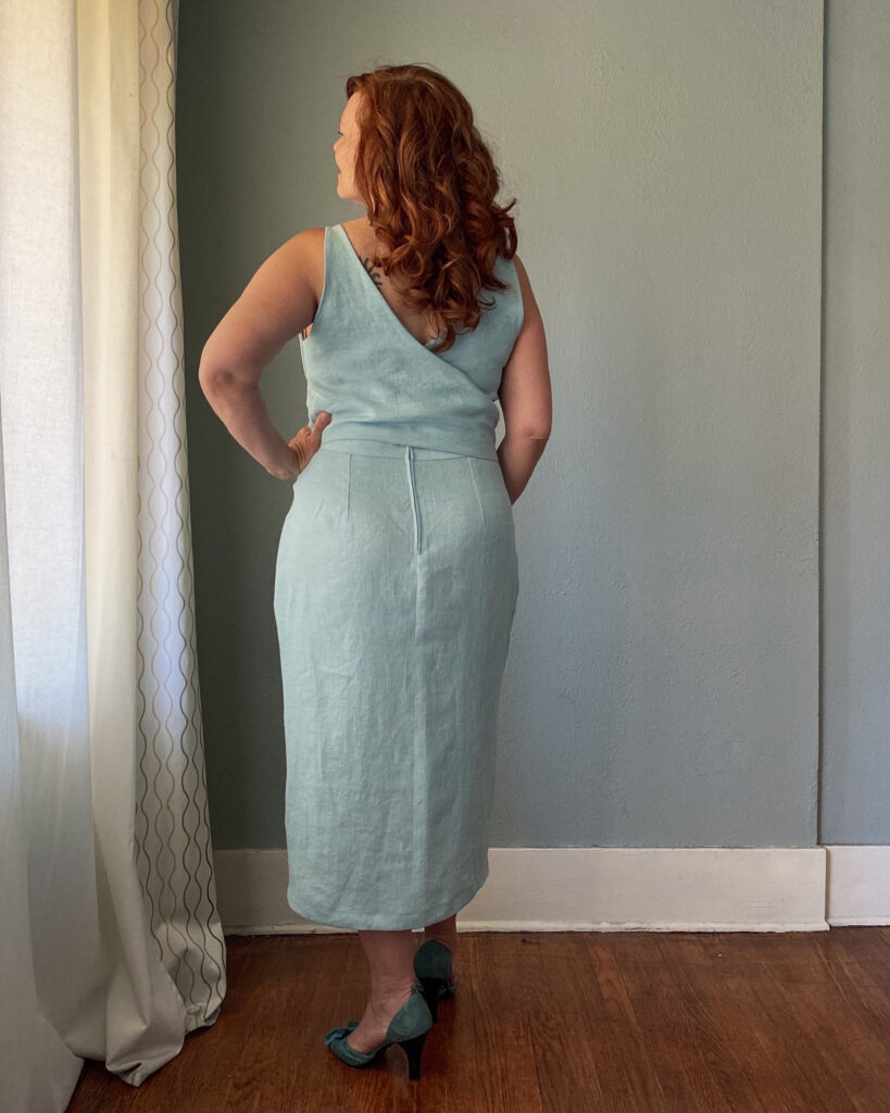 A mid-50s woman with red hair stands against a grey wall wearing a handmade light blue sundress.