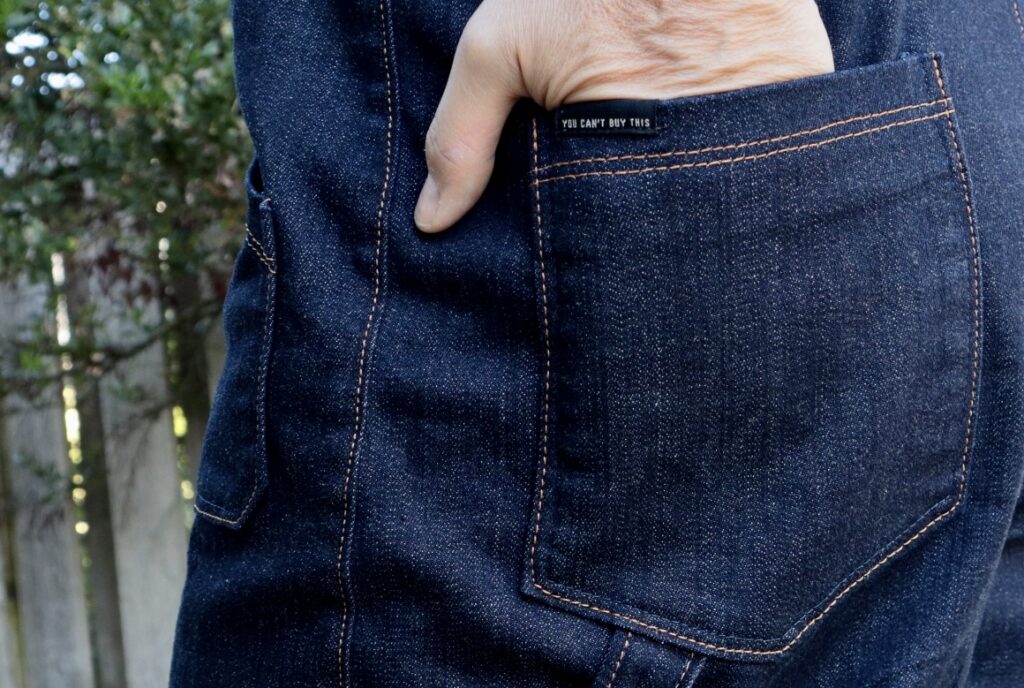 Close up of back pocket on denim overalls with black and white label reading "You can't buy this".