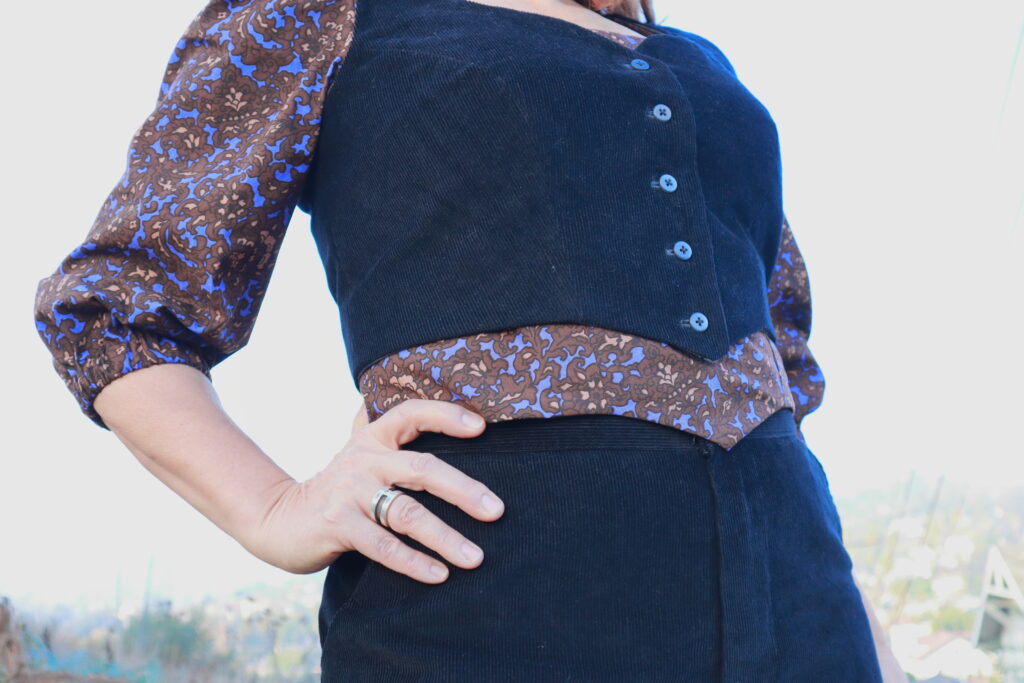 Detail of black corduroy vest with purple printed blouse.