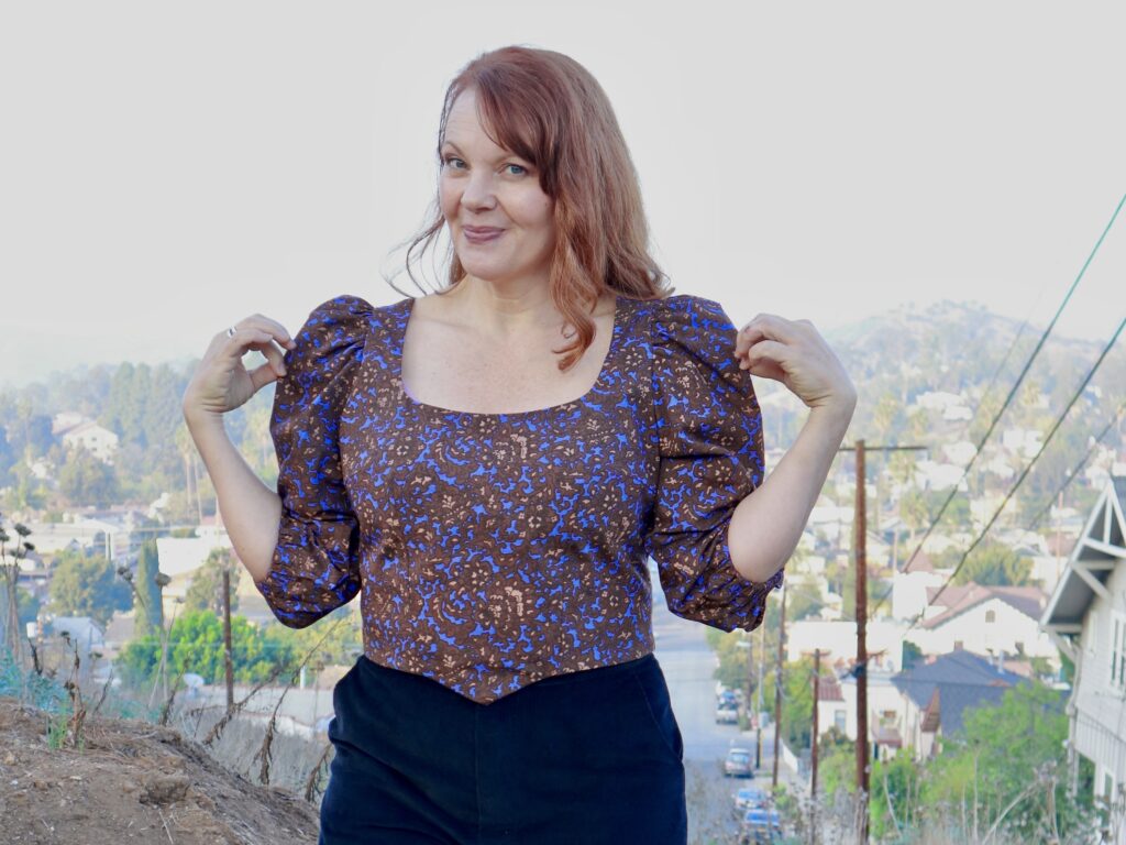 A red-haired woman wears a poufy-sleeved purple print blouse.