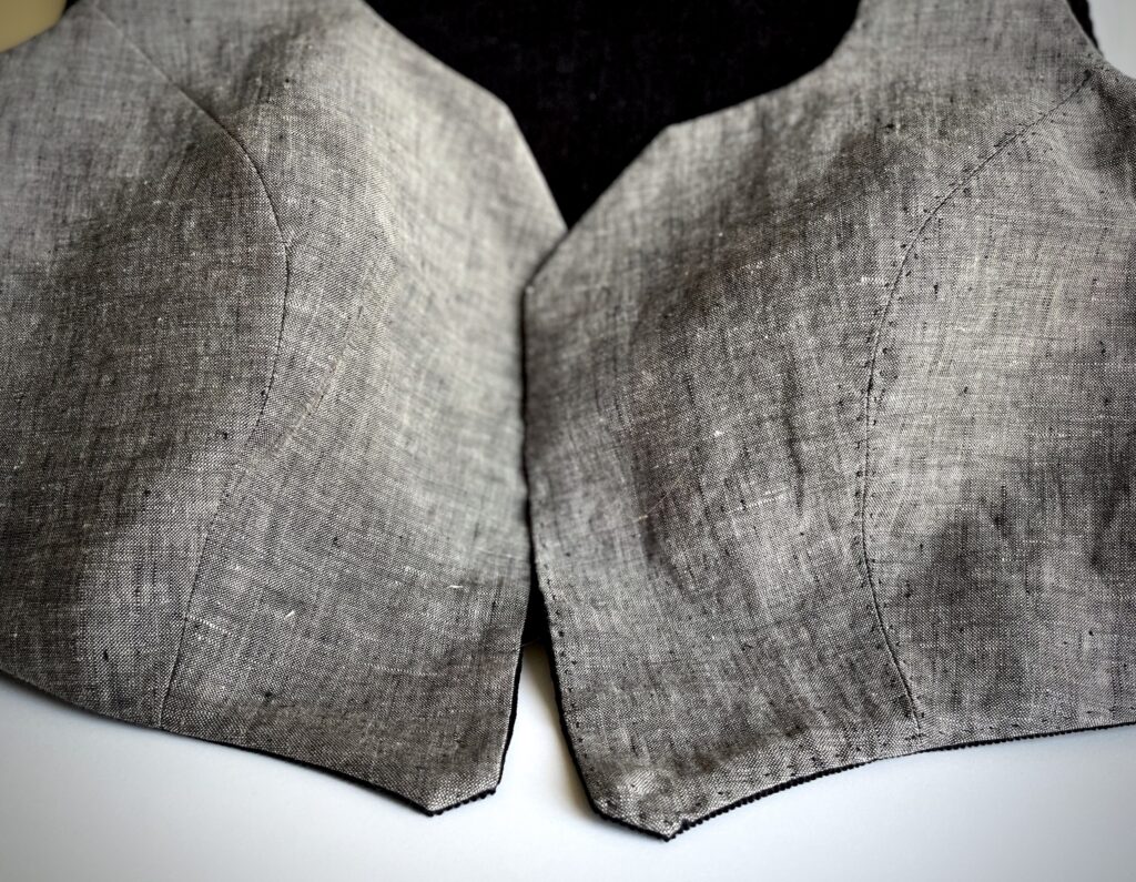 Detail of grey vest with black pick stitching.