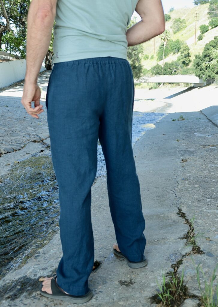 Back waist-down view of a white man standing in a dry riverbed wearing dark blue pants 