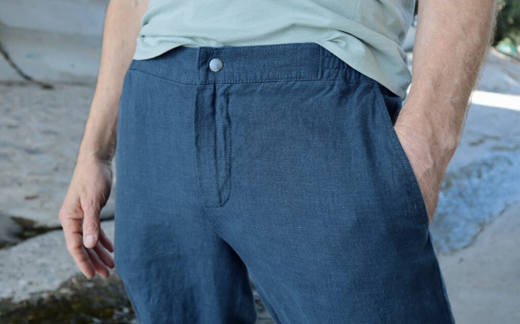 Close up of dark blue pants with snap and zipper fly and partly elasticized waistband.