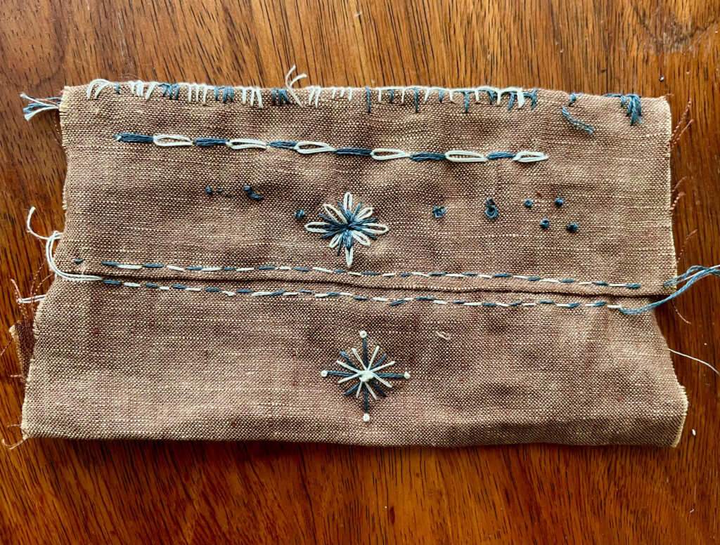 Detail of white and grey embroidery stitches on brown linen
