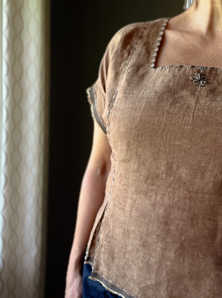Close up of a brown embroidered linen top and large beaded earrings