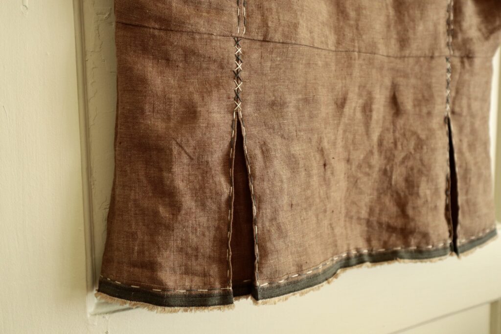 Close up of bottom half of brown linen top with grey and white embroidery stitches
