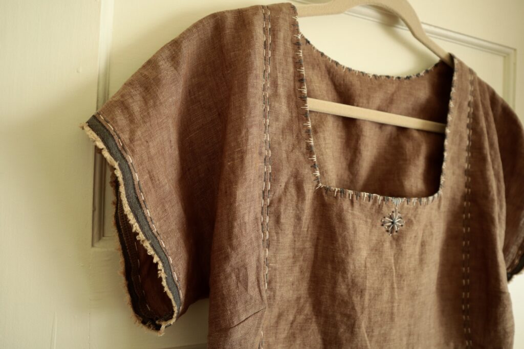 Close up of top half of brown linen top with grey and white embroidery at neckline and sleeve