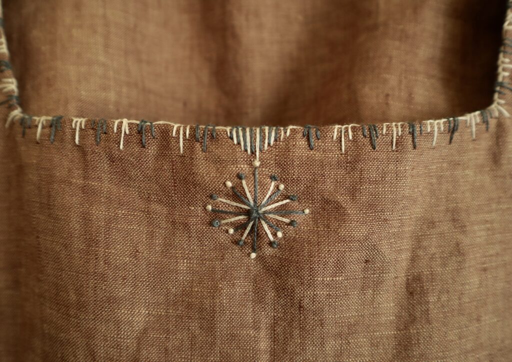 Detail of white and grey embroidery on neckline edge of brown linen top